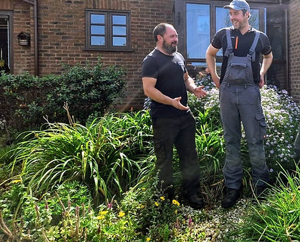 Two members of the Jay's Garden Maintenance team standing in a garden beside a brick building